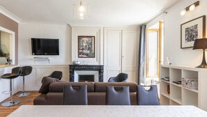 A modern living room with a sofa, chairs, a fireplace, a TV, and a bookshelf.