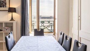 A dining area with a marble table, black chairs, a lamp, a bookshelf, and a view of the city through a large window.