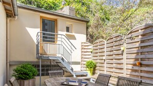 A wooden deck with a round table and chairs, a staircase leading to a building, and a wooden fence.