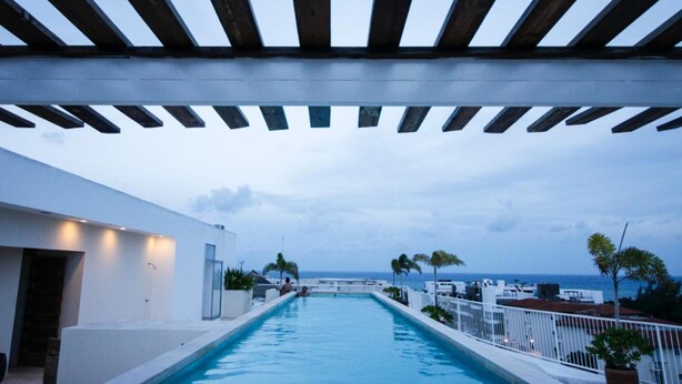Ein Poolbereich mit Meerblick, einer Holzpergola und einem weißen Gebäude.