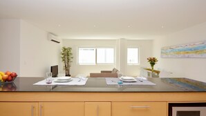 A modern kitchen with a central island, wooden cabinets, and a dining area with a sofa and table. - Stylish 2BR a few steps to the beach with pools by Happy Address (Playa del Carmen)