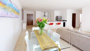 A modern dining area with a glass table, a vase with flowers, and a beige runner. - Stylish 2BR a few steps to the beach with pools by Happy Address (Playa del Carmen)
