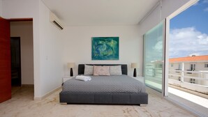 A bedroom with a large bed, a painting on the wall, and a view of buildings through a glass door. - Stylish 2BR a few steps to the beach with pools by Happy Address (Playa del Carmen)