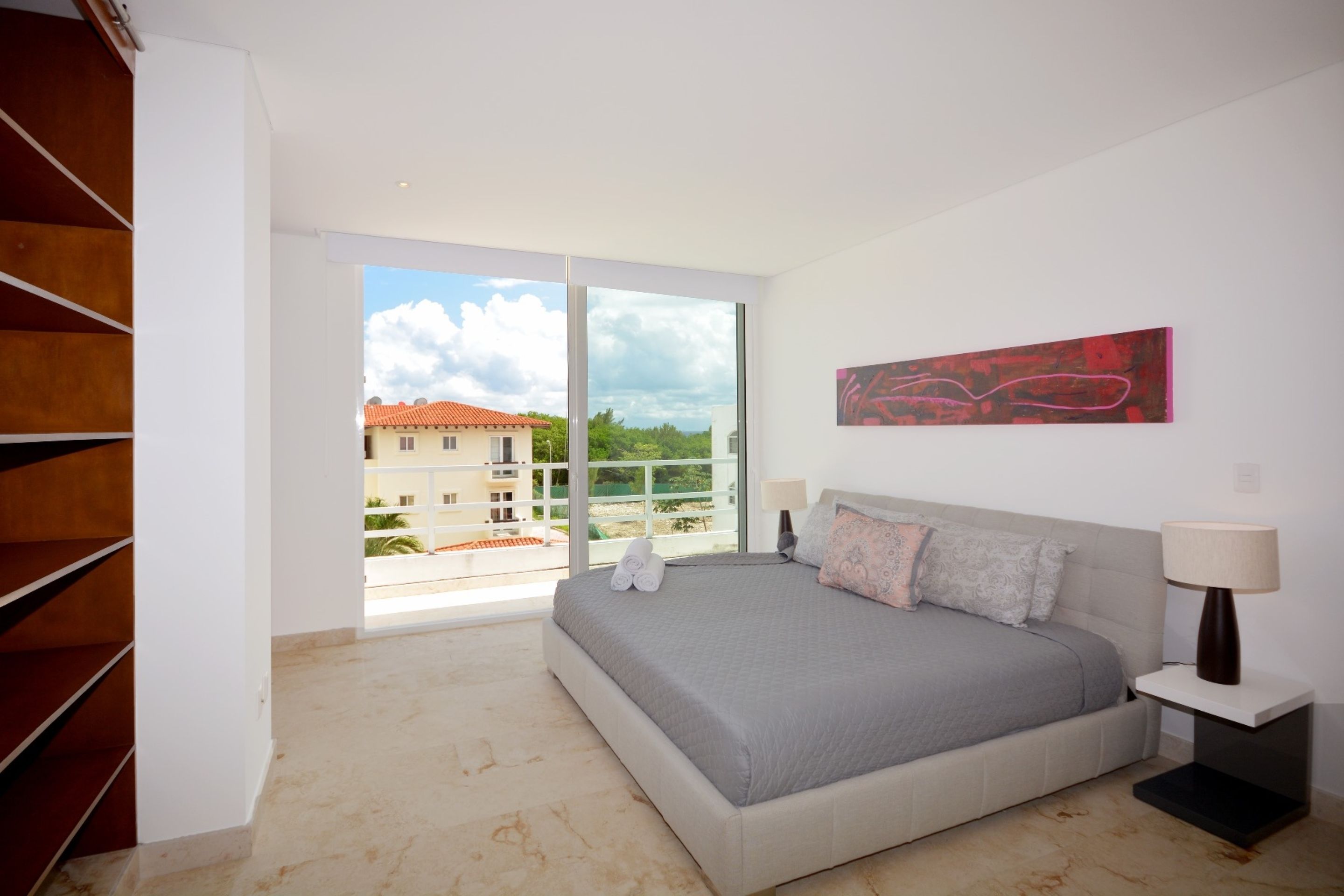 Ein Schlafzimmer mit einem großen Bett, einem Nachttisch, einem Fenster mit Blick auf Gebäude und einer Treppe.