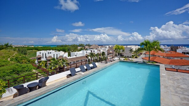 A swimming pool with lounge chairs, a view of the ocean, and buildings in the background. - Stylish 2BR a few steps to the beach with pools by Happy Address (Playa del Carmen)