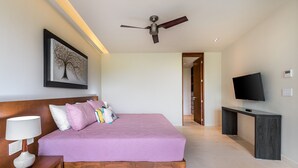 Ein modernes Schlafzimmer mit einem großen Bett, einem Deckenventilator, einem Flachbildfernseher und einem Gemälde an der Wand.