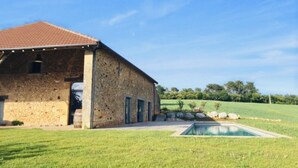 A stone building with a red-tiled roof, a swimming pool, and a grassy lawn.