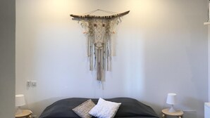 A modern bedroom with a dark grey bed, two decorative pillows, a wall hanging, and bedside lamps.