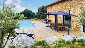 A poolside area with a stone building, lounge chairs, and a wooden deck.
