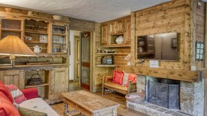 Ein rustikales Interieur mit Holzwänden, Kamin, Fernseher und einer gemütlichen Sitzecke.