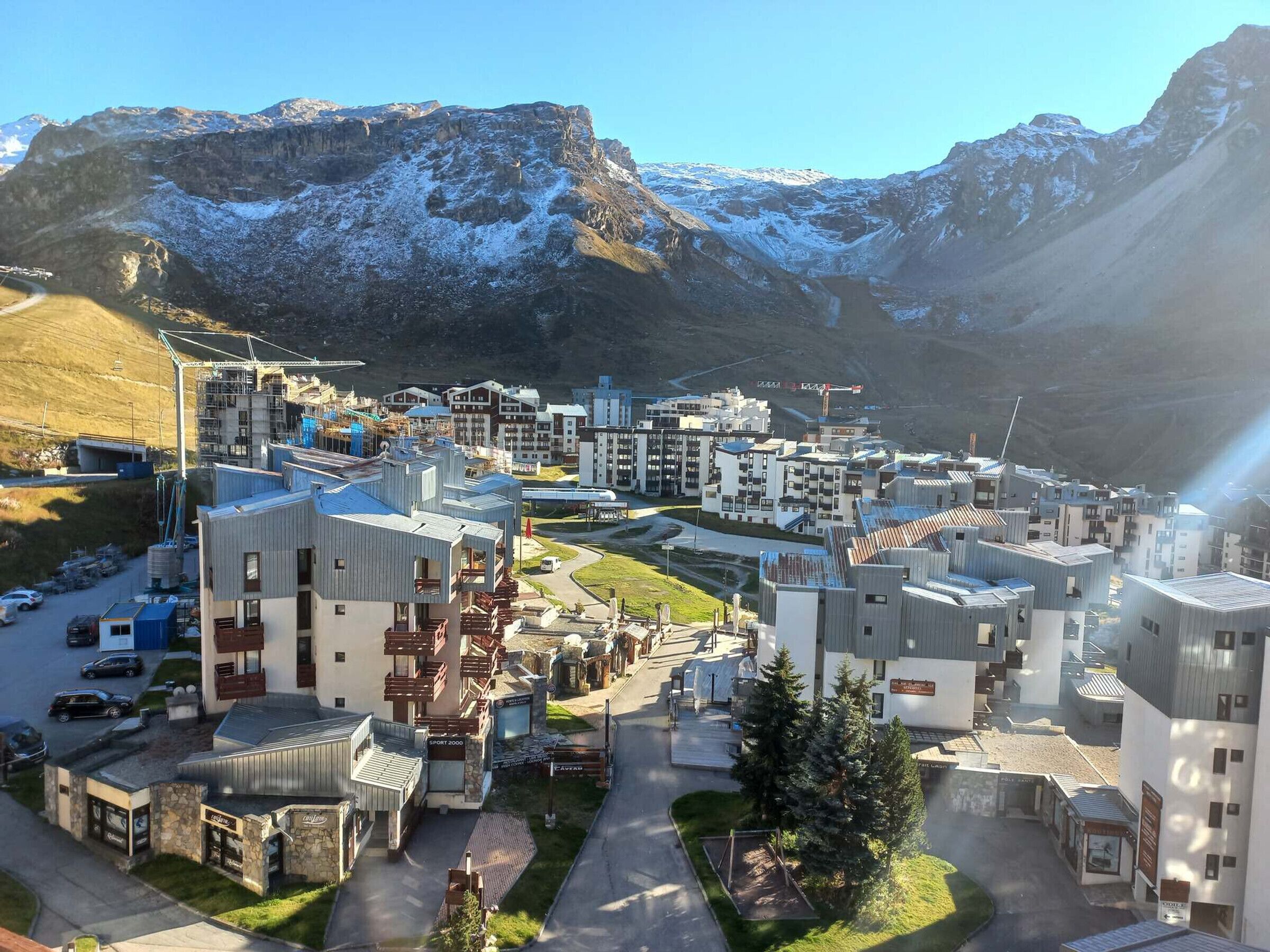 A modern hotel complex with multiple buildings, a parking area, and a mountainous backdrop.