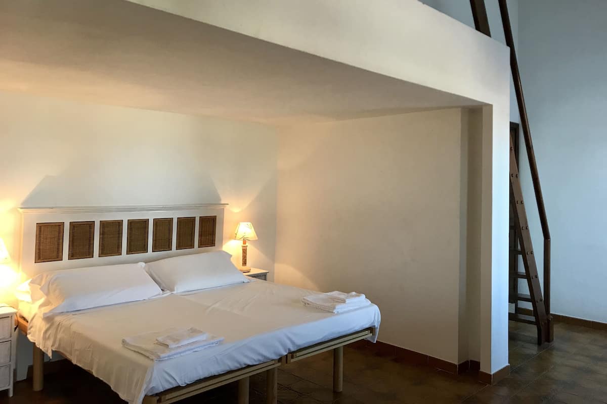 Una cama bien tendida en una habitación con techo alto y una escalera de madera.