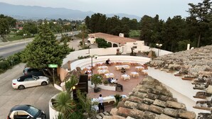A courtyard with outdoor seating, a car parked nearby, and a view of distant mountains. - Hotel Su Meriagu (Quartu Sant'Elena)