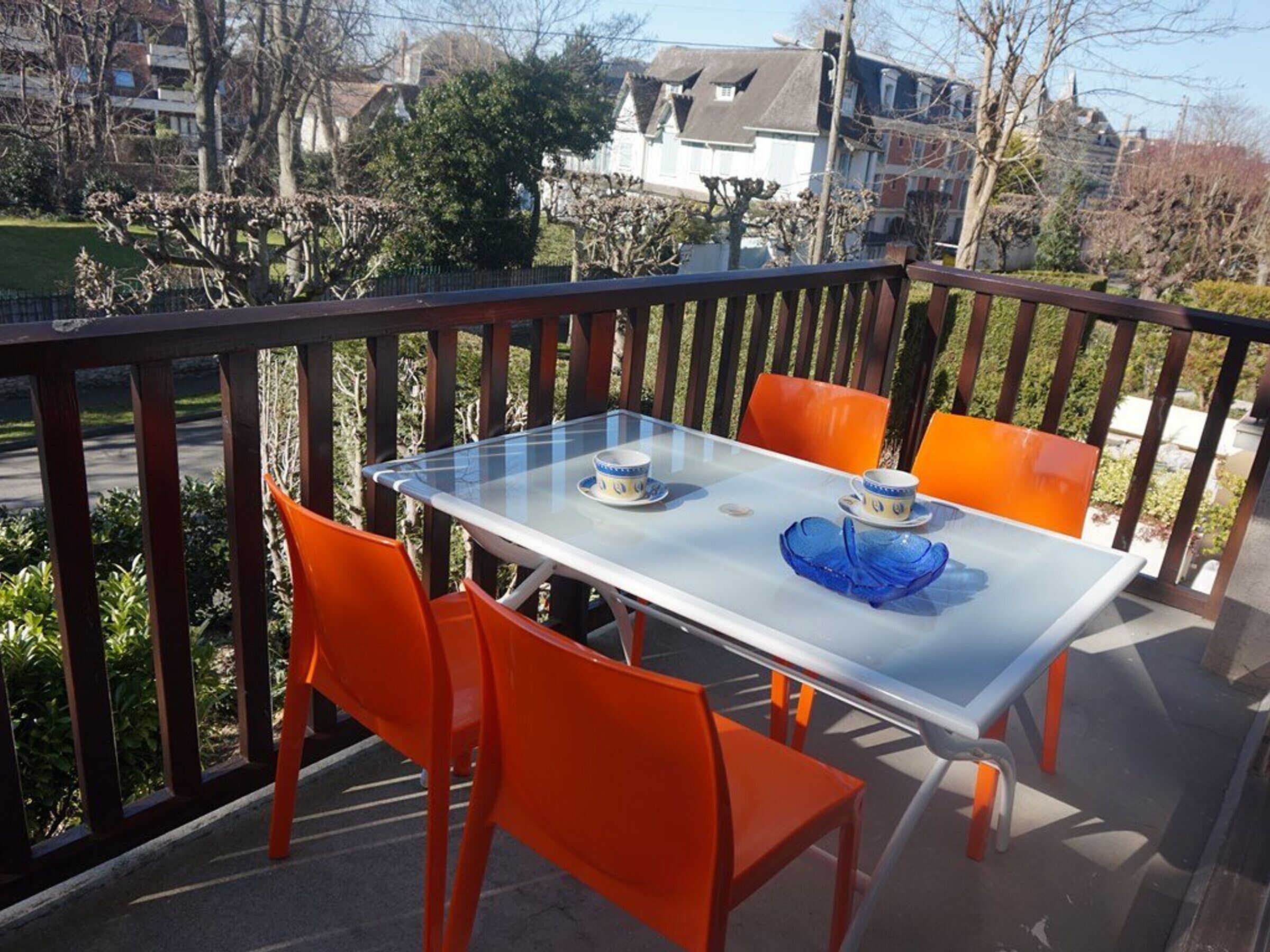 A glass-top table with two orange chairs on a balcony with a wooden railing.