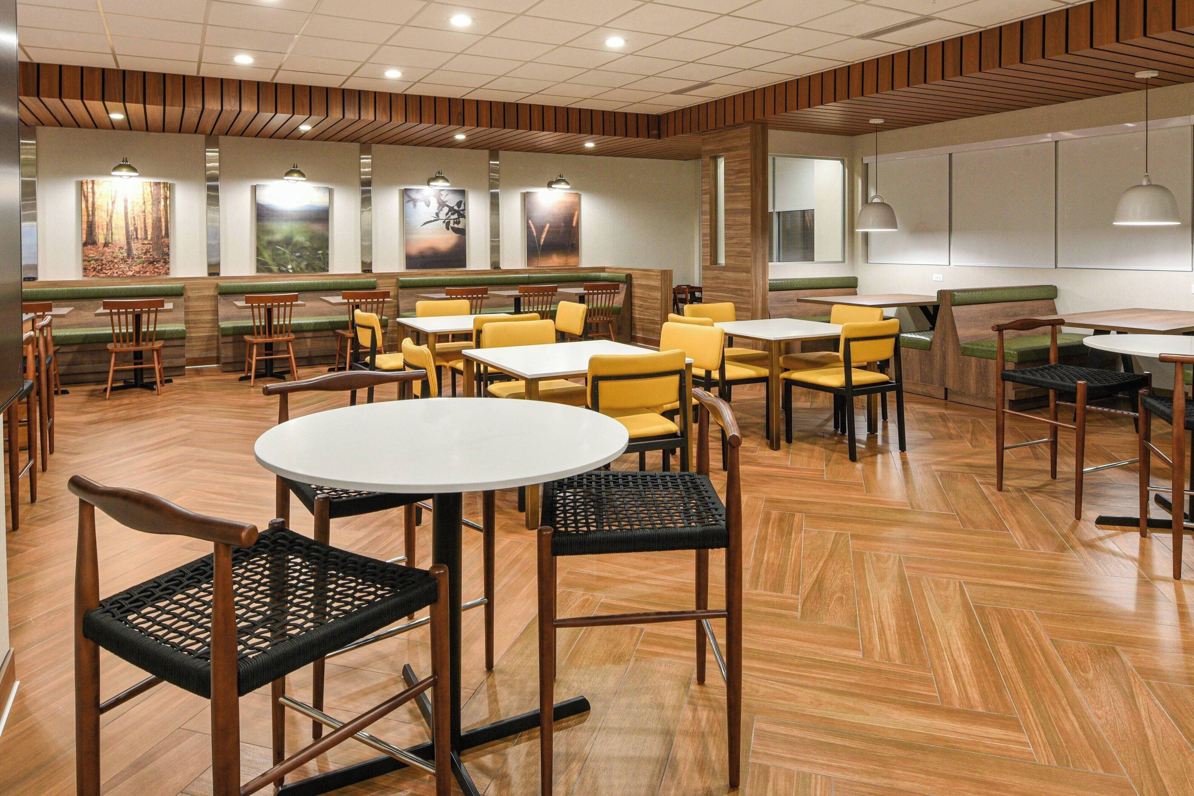 Un restaurante con suelo de madera, asientos tapizados en tonos verdes y sillas amarillas.