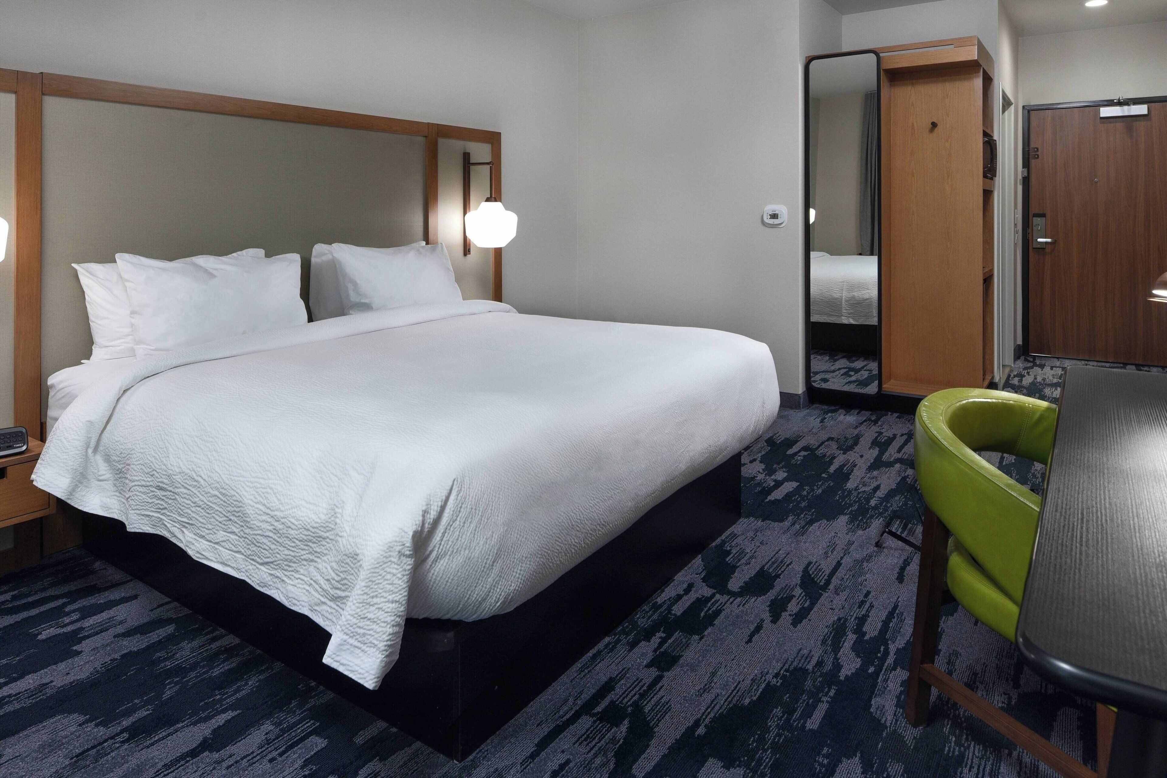 A hotel room with a large bed, a green chair, a desk, and a wardrobe.