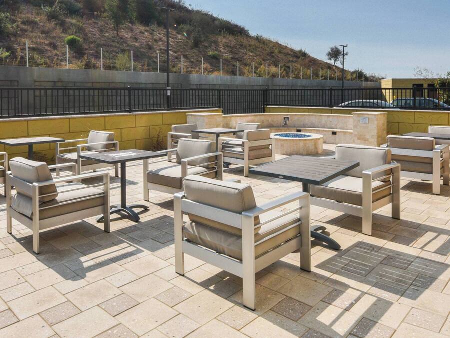 An outdoor patio with multiple seating areas, including sofas and tables, arranged on a tiled floor.