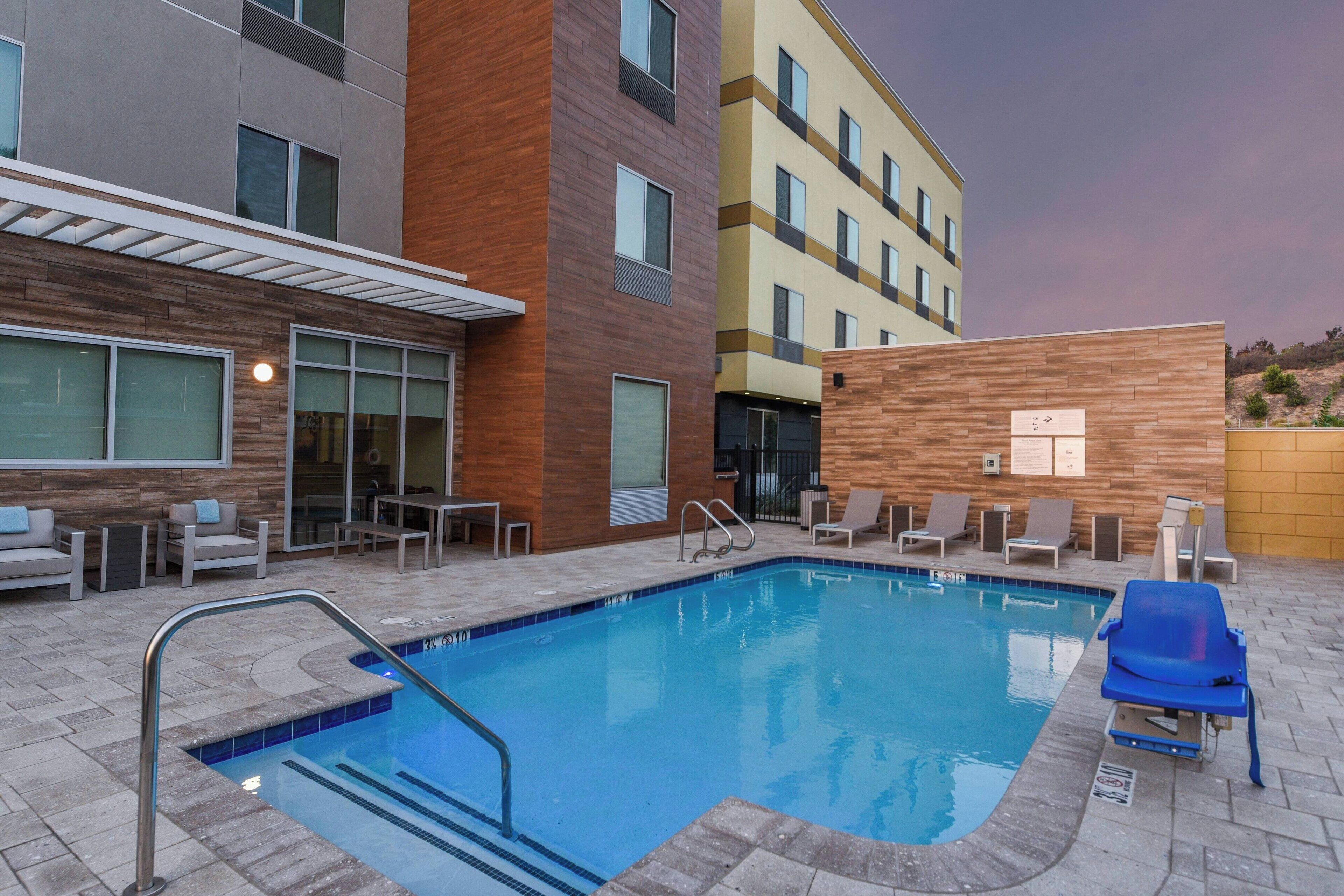 A modern hotel pool area with a clear pool, lounge chairs, and a wooden facade.