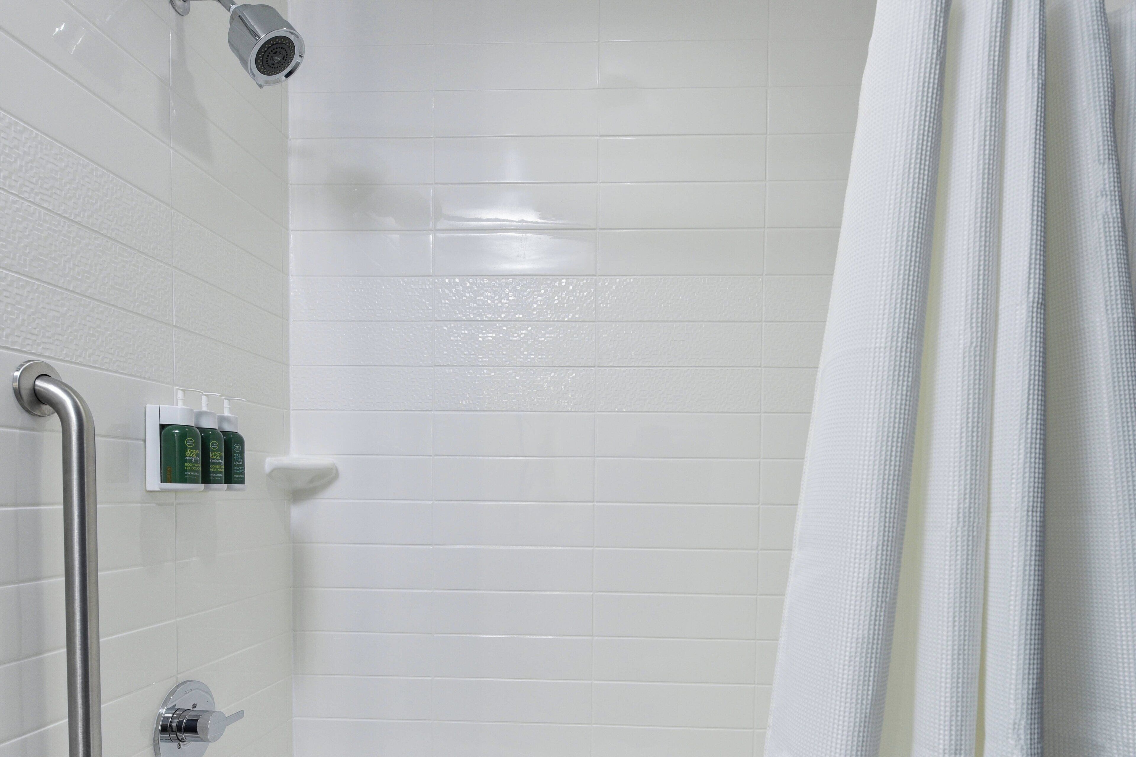A shower area with white tiles, a showerhead, a handrail, and a set of toiletries.