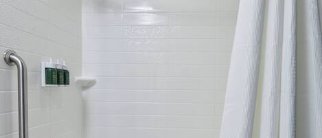 A shower area with white tiles, a showerhead, a handrail, and a set of toiletries.