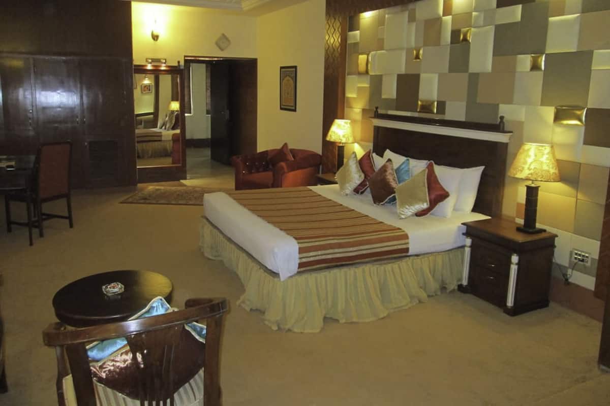 Ein Hotelzimmer mit einem großen Bett, einer Sitzecke mit einem Sessel, einem kleinen Tisch und einem Spiegel.