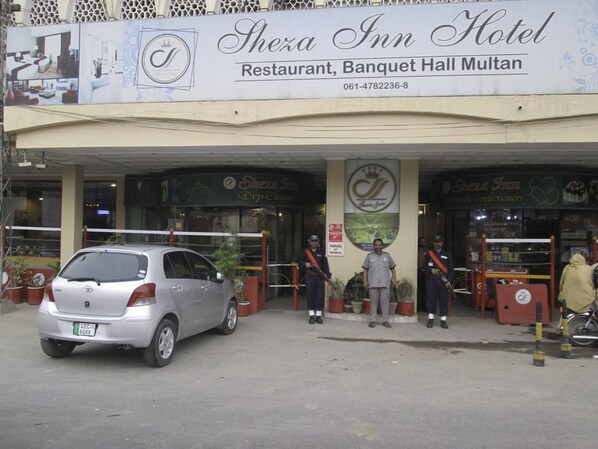 The exterior of Shexa Inn Hotel with a parked car and security personnel standing in front.
