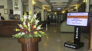 A reception area with a large flower arrangement in a wooden planter, a reception desk, and a digital screen displaying an event announcement. - Sheza Inn Hotel Multan (Multan)