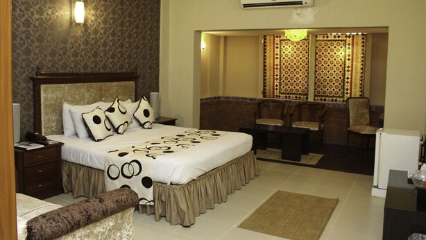A hotel room with a large bed, a desk, a chair, and a small table. There is an air conditioning unit on the wall. - Sheza Inn Hotel Multan (Multan)