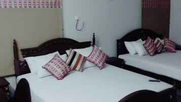 A hotel room with two beds, each with a wooden headboard, white bedding, and patterned pillows. An air conditioning unit is mounted on the wall above the beds.