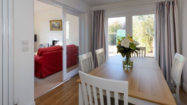 A dining area with a wooden table, white chairs, and a vase of flowers. - Glenconner Garden Cottage (North Berwick)