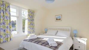 A bedroom with a bed, two bedside tables, a nightstand, a window with curtains, and a ceiling light fixture. - Glenconner Garden Cottage (North Berwick)