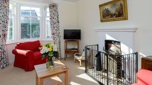 A living room with a red sofa, a TV, a fireplace, and a painting on the wall. - Glenconner Garden Cottage (North Berwick)