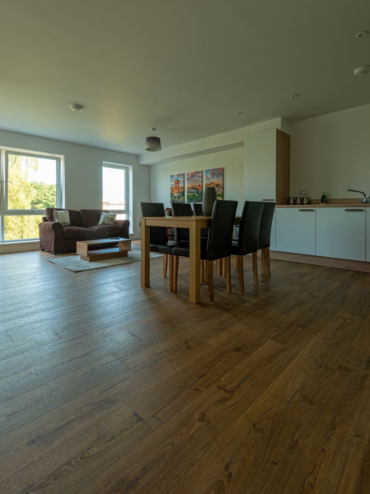 A modern living room with a wooden dining table and chairs, a sofa, and a large window.