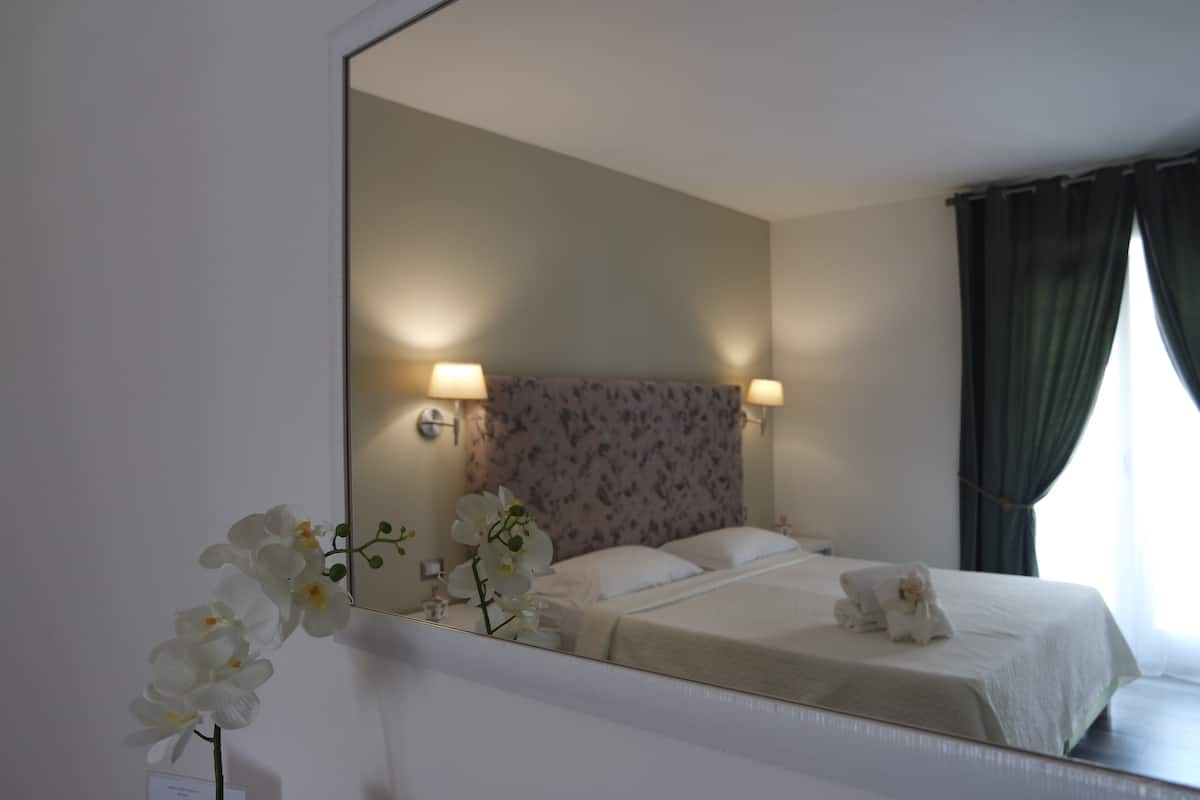 Quarto de hotel com uma cama, um espelho e uma luminária fixada na parede.