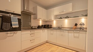 A modern kitchen with white cabinets, a stainless steel range hood, a microwave, and a coffee maker. - Spacious Modern Apartment (Edinburgh)