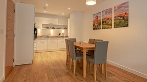 A modern kitchen with white cabinets, a wooden dining table with four chairs, and a pendant light. There are three framed pictures on the wall. - Spacious Modern Apartment (Edinburgh)