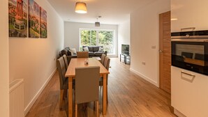 A modern apartment with a dining area, a living room with a sofa and TV, and a kitchen with a built-in oven. - Spacious Modern Apartment (Edinburgh)