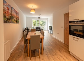 Enjoy a comfortable stay in this stylish apartment with a spacious living area, dining table for four, and a large window offering a view of lush greenery.