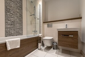 Et moderne badeværelse med et glasafskærmet brusebad, et træbordplads og et hvidt toilet.