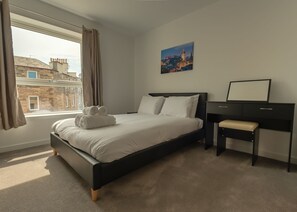 Et moderne hotelværelse med en seng, et skrivebord og udsigt til bybilledet gennem vinduet.