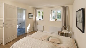 Ein Schlafzimmer mit einem Bett, einem Schreibtisch, einem Stuhl, einem Fenster und einem durch eine offene Tür einsehbaren Badezimmer.