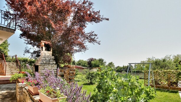 Un jardin avec des plates-bandes surélevées, une structure en pierre et un ensemble de jeux avec une balançoire.