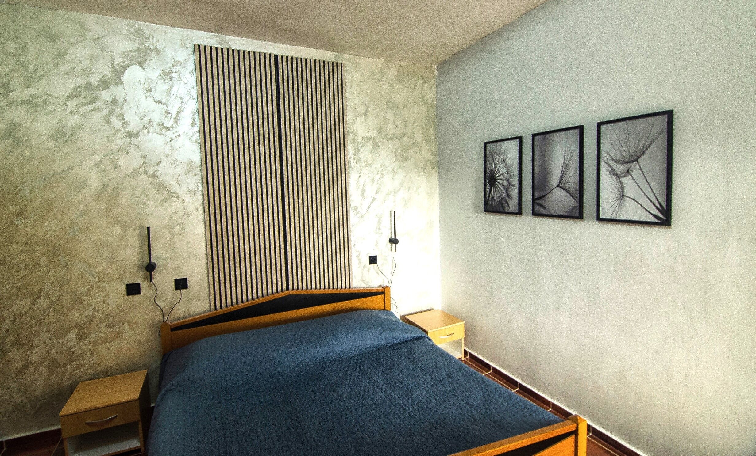 A bedroom with a bed, bedside tables, a wall-mounted radiator, and three framed pictures.