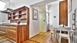 A modern kitchen with wooden cabinetry, a central island, and a dining area with white chairs and a table. - A one bedroom semibasement apartment - Lana 2 (Petrovija)
