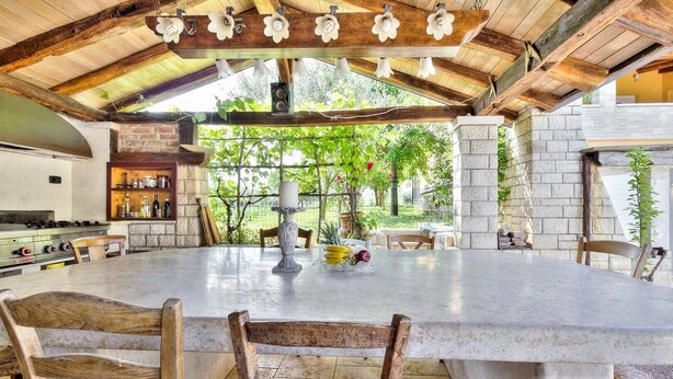 An outdoor kitchen with a large island, stone walls, and wooden furniture. - A one bedroom semibasement apartment - Lana 2 (Petrovija)