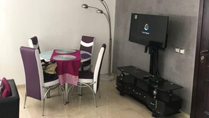 Un espace de vie compact comprenant une table à manger, des chaises, un téléviseur à écran plat et un meuble de rangement noir pour les appareils multimédias.