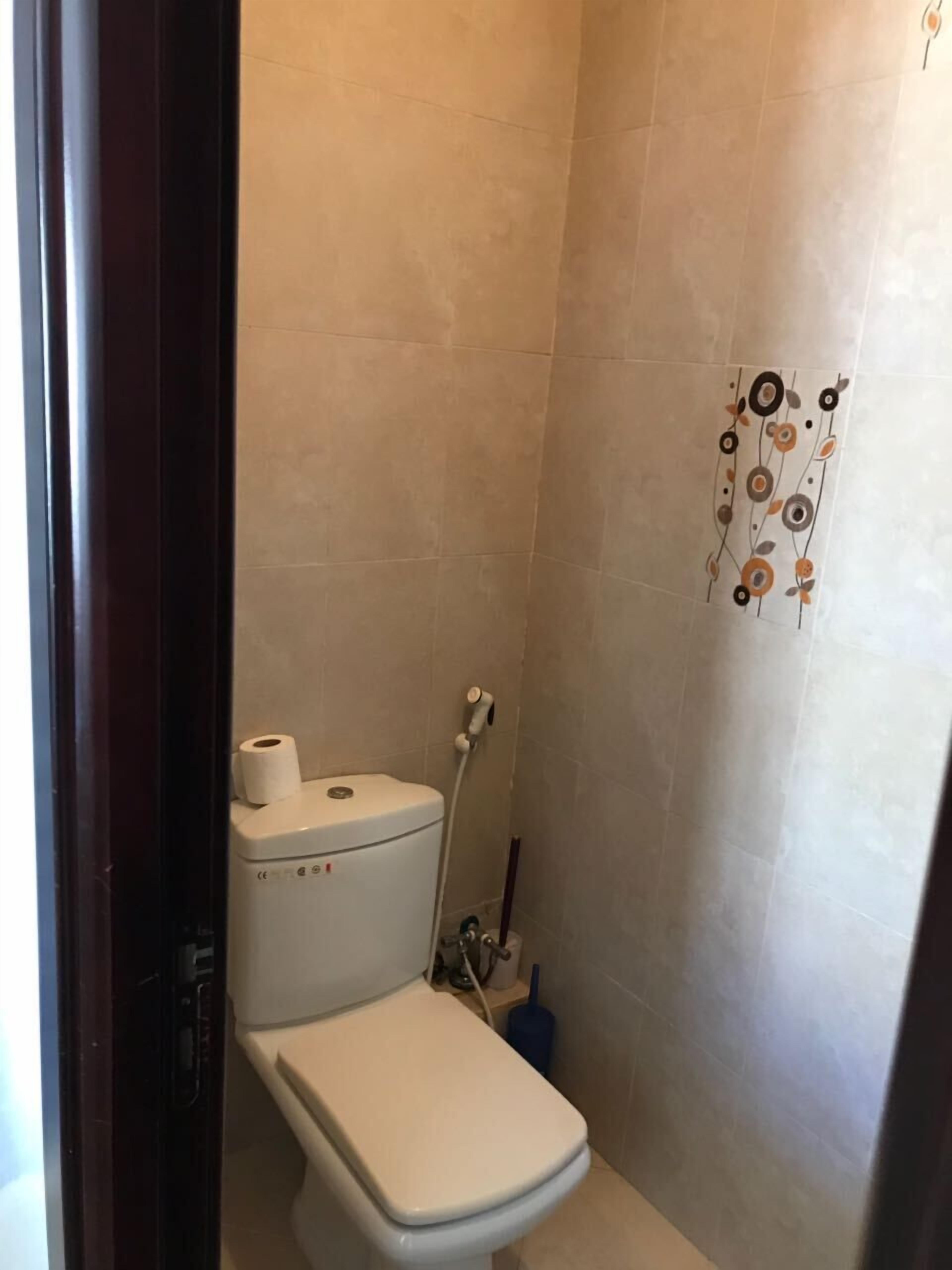 Ein kleines, kompaktes Badezimmer mit Toilette, Dusche und einem an der Wand befestigten Toilettenpapierhalter.