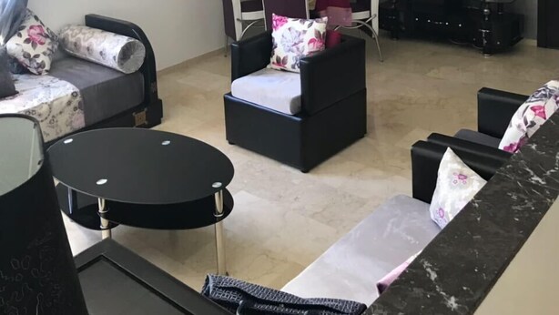 Un salon moderne comprenant un ensemble de canapés, une petite table ronde, une table basse noire et un téléviseur à écran plat fixé au mur.