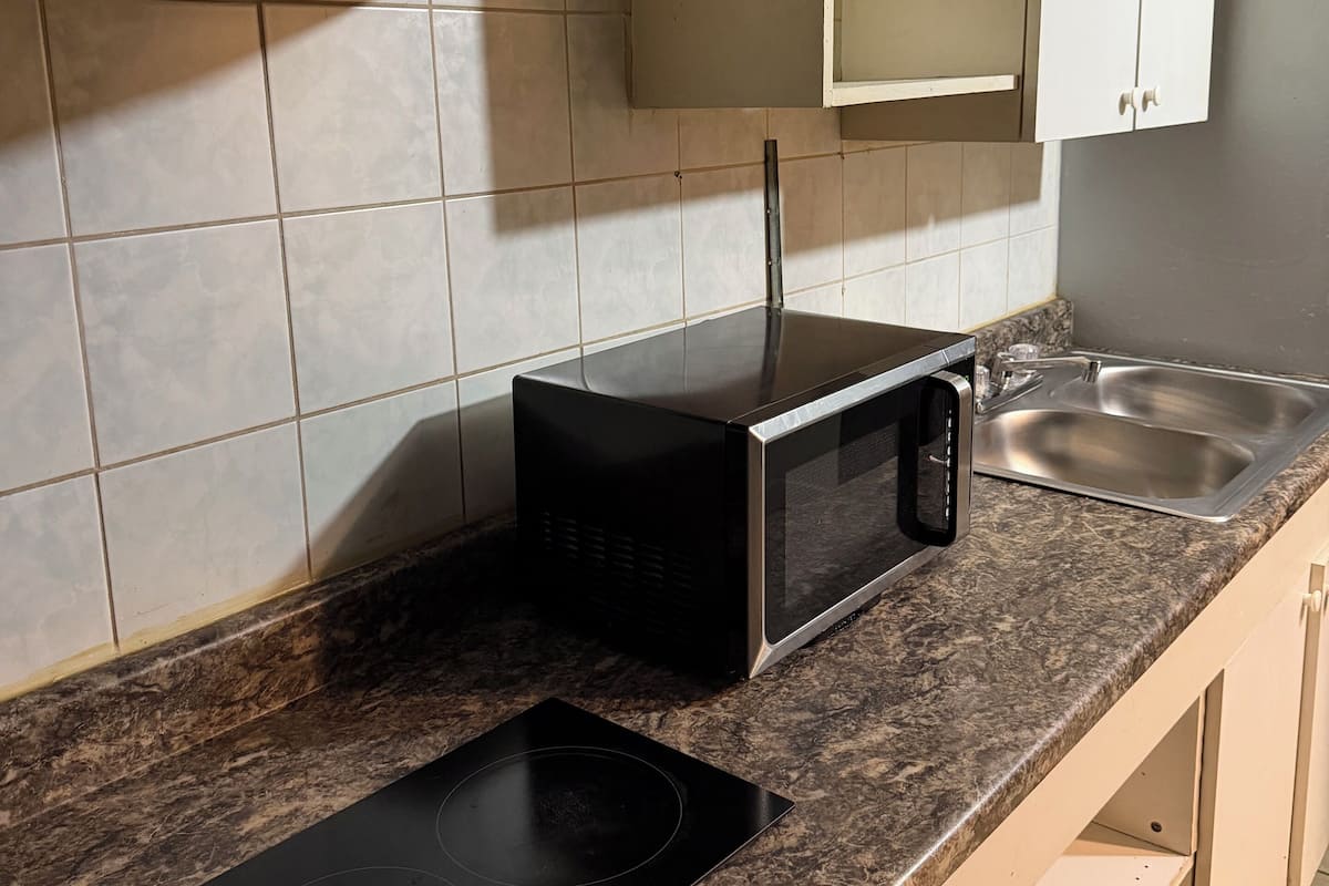 A kitchen with white cabinets, a microwave, a sink, and a black induction cooktop.