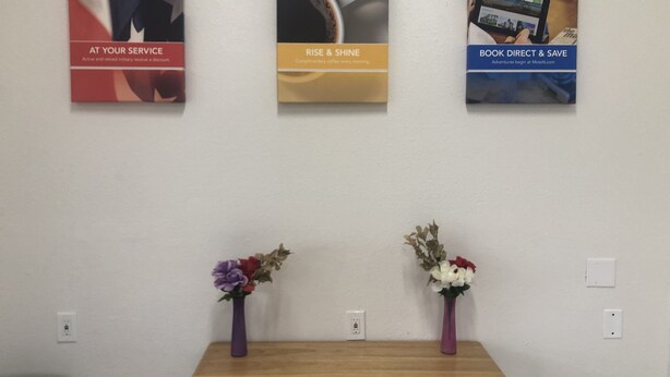 Three promotional posters on a wall, a wooden table with two vases of flowers, and a white wall with electrical outlets. - Troy Inn and Suites (Troy)